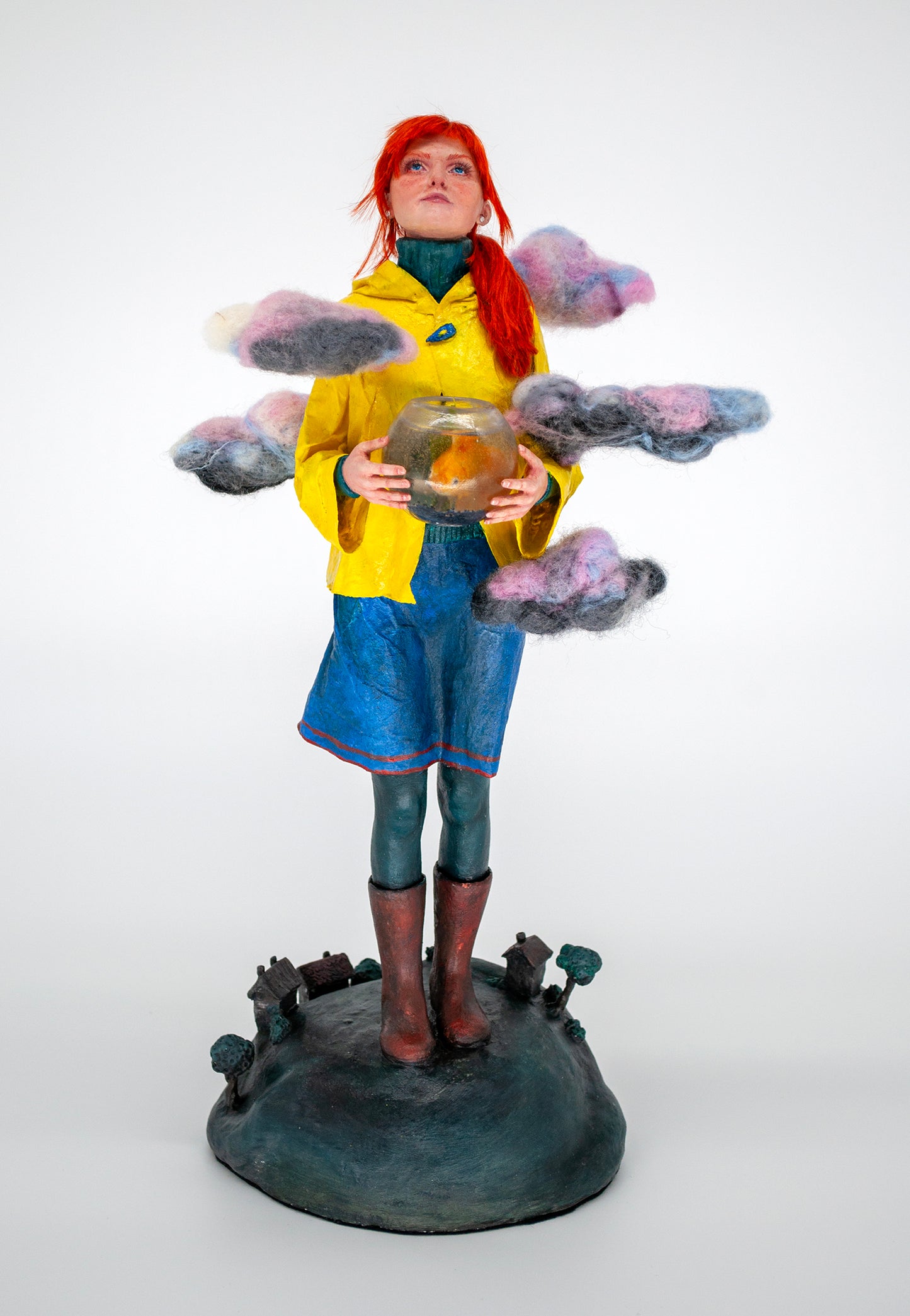 Realistic sculpture of a girl with red hair wearing a yellow raincoat holding a fishbowl above the world