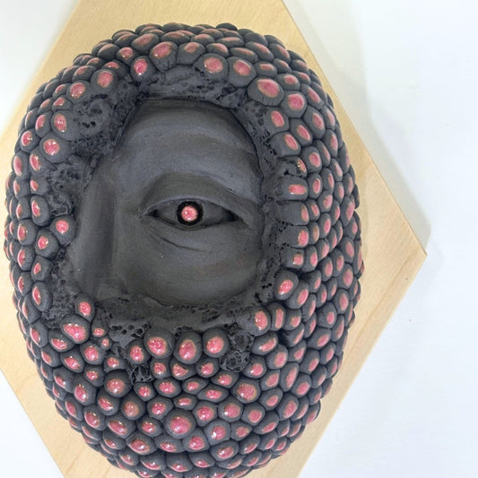 Surrealist black stoneware clay wall hanging combining facial features and berries