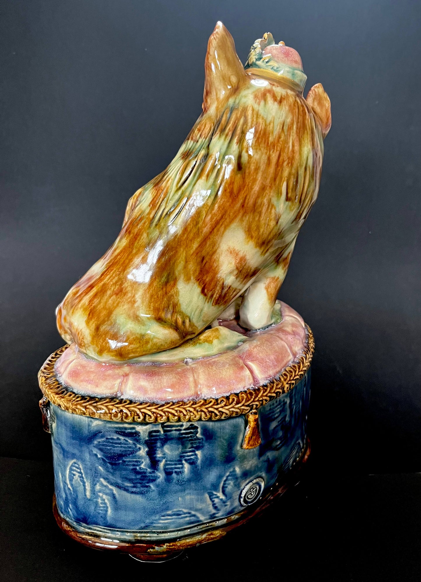 A glazed ceramic figurine of a cat on a round blue and pink decorative base.