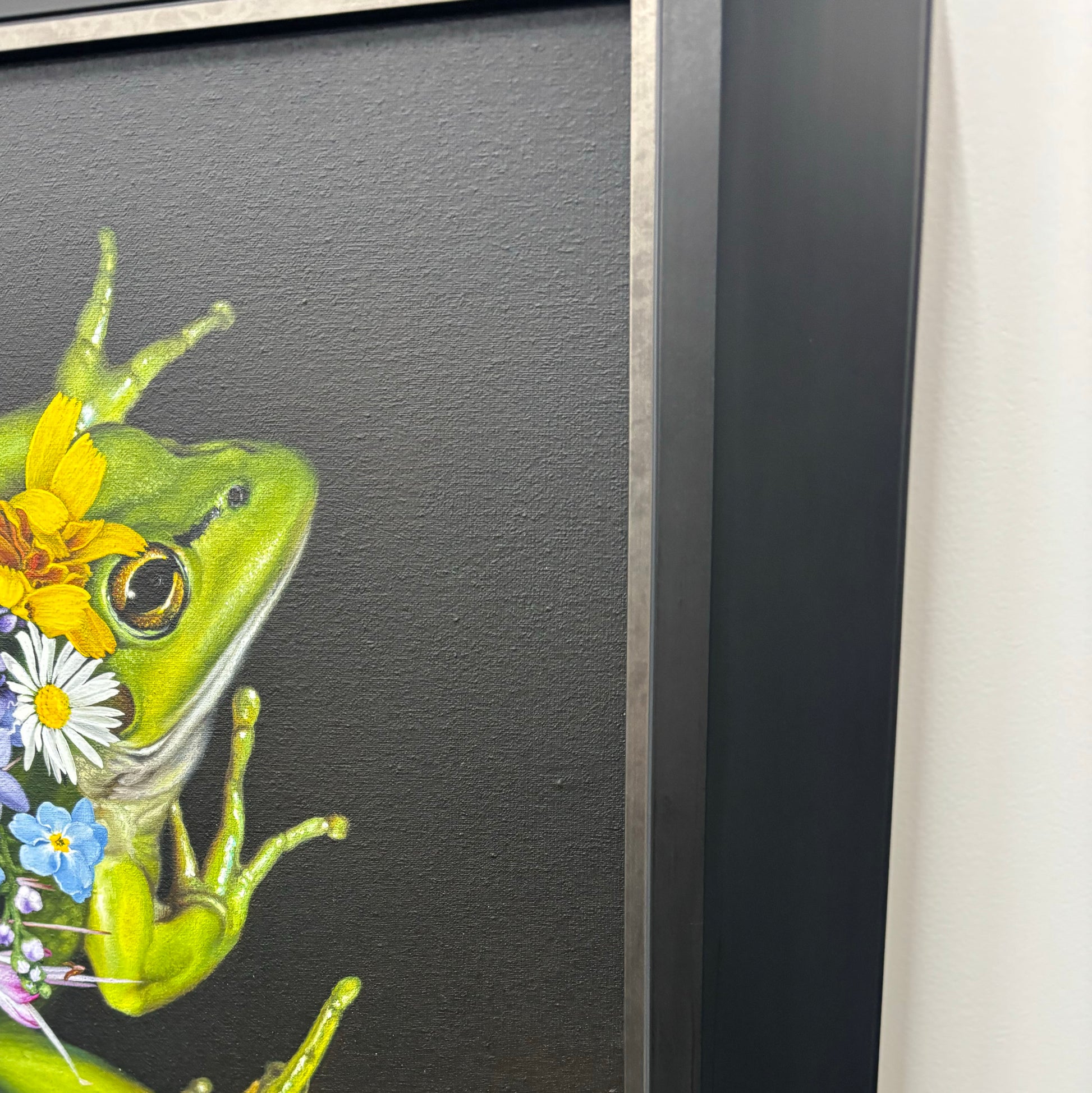 Framed artwork of a green frog with flowers on a dark background