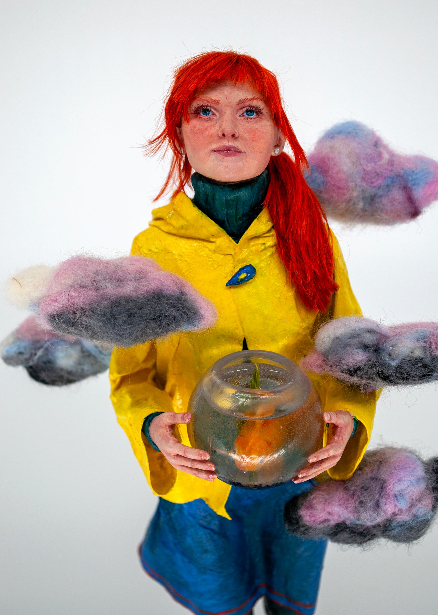 Realistic sculpture of a girl with red hair wearing a yellow raincoat holding a fishbowl above the world