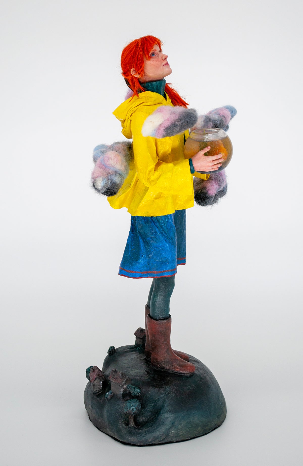 Realistic sculpture of a girl with red hair wearing a yellow raincoat holding a fishbowl above the world
