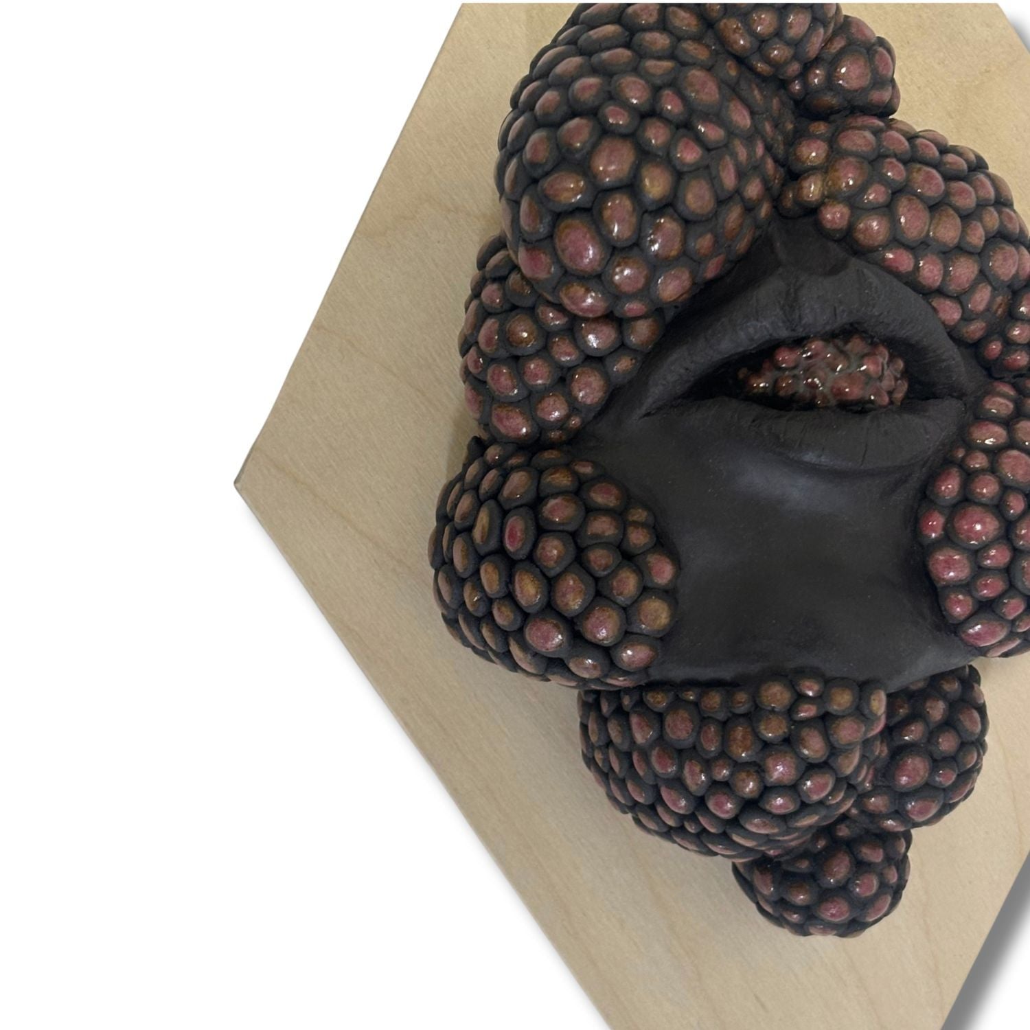 Surrealist black stoneware clay wall hanging combining facial features and berries