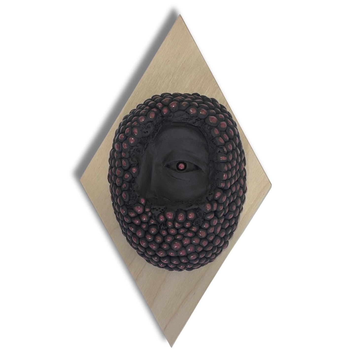 Surrealist black stoneware clay wall hanging combining facial features and berries