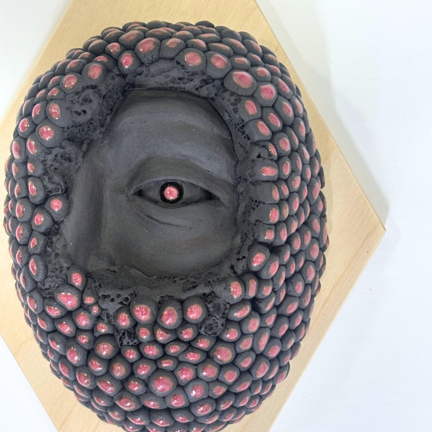 Surrealist black stoneware clay wall hanging combining facial features and berries