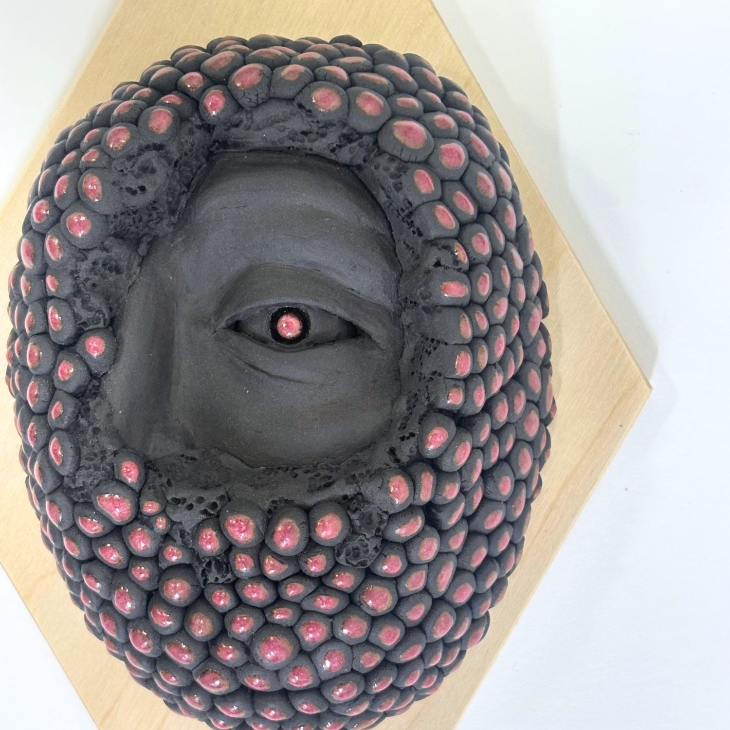 Surrealist black stoneware clay wall hanging combining facial features and berries