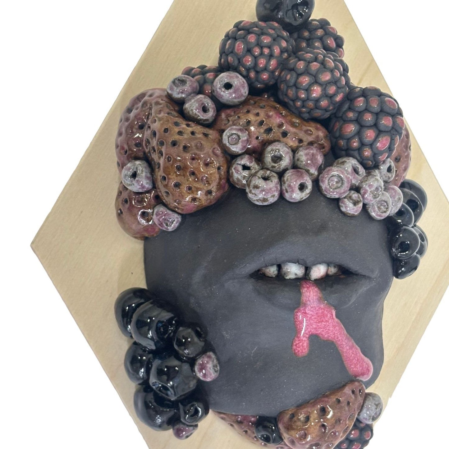 Surrealist black stoneware clay wall hanging combining facial features and berries