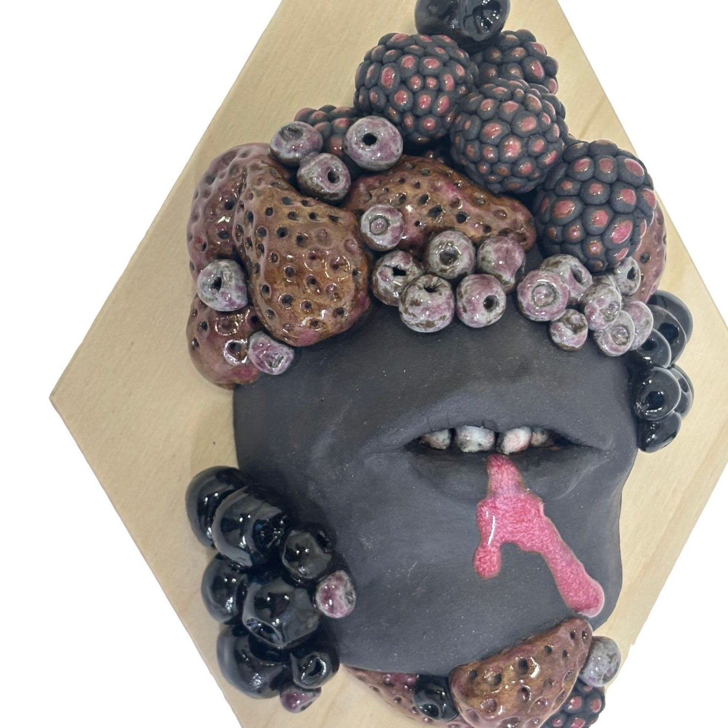Surrealist black stoneware clay wall hanging combining facial features and berries