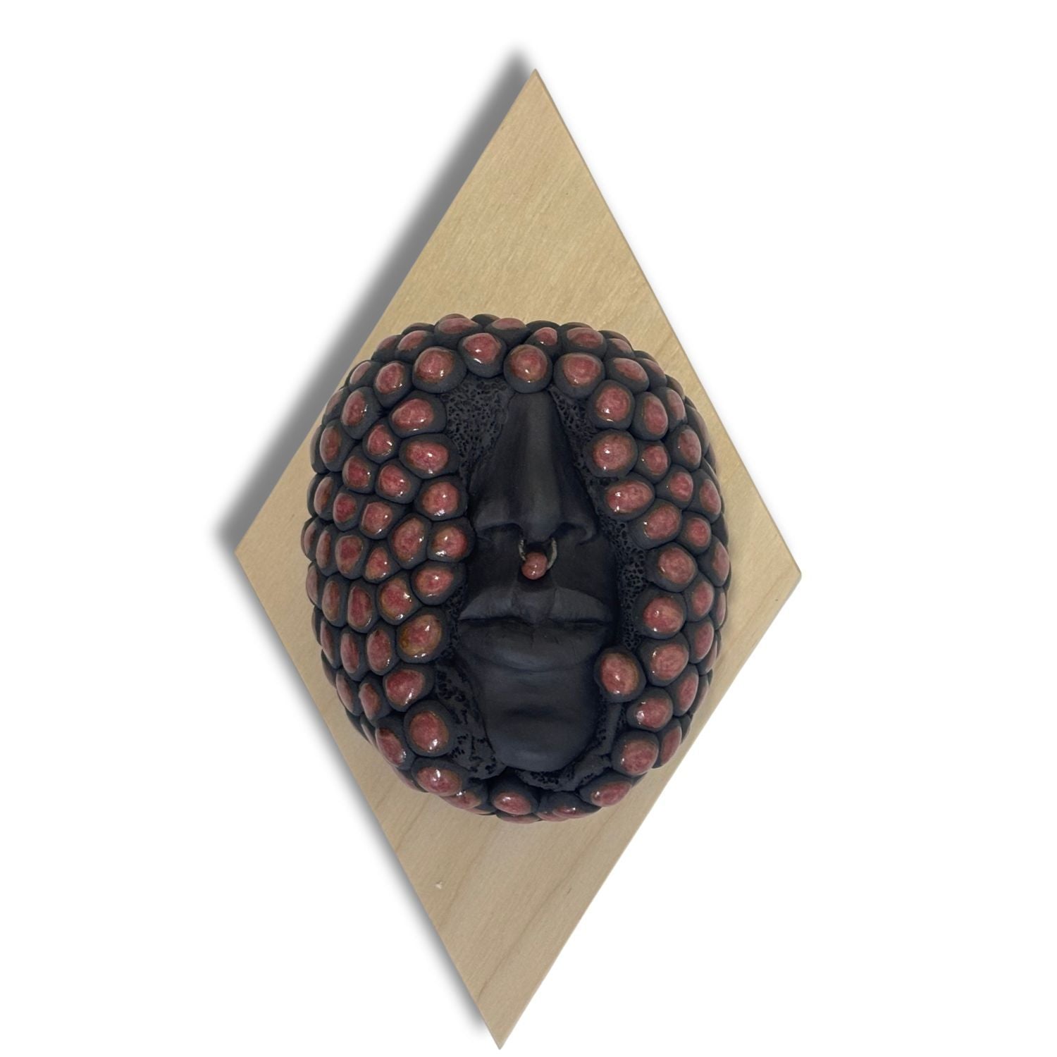Surrealist black stoneware clay wall hanging combining facial features and berries