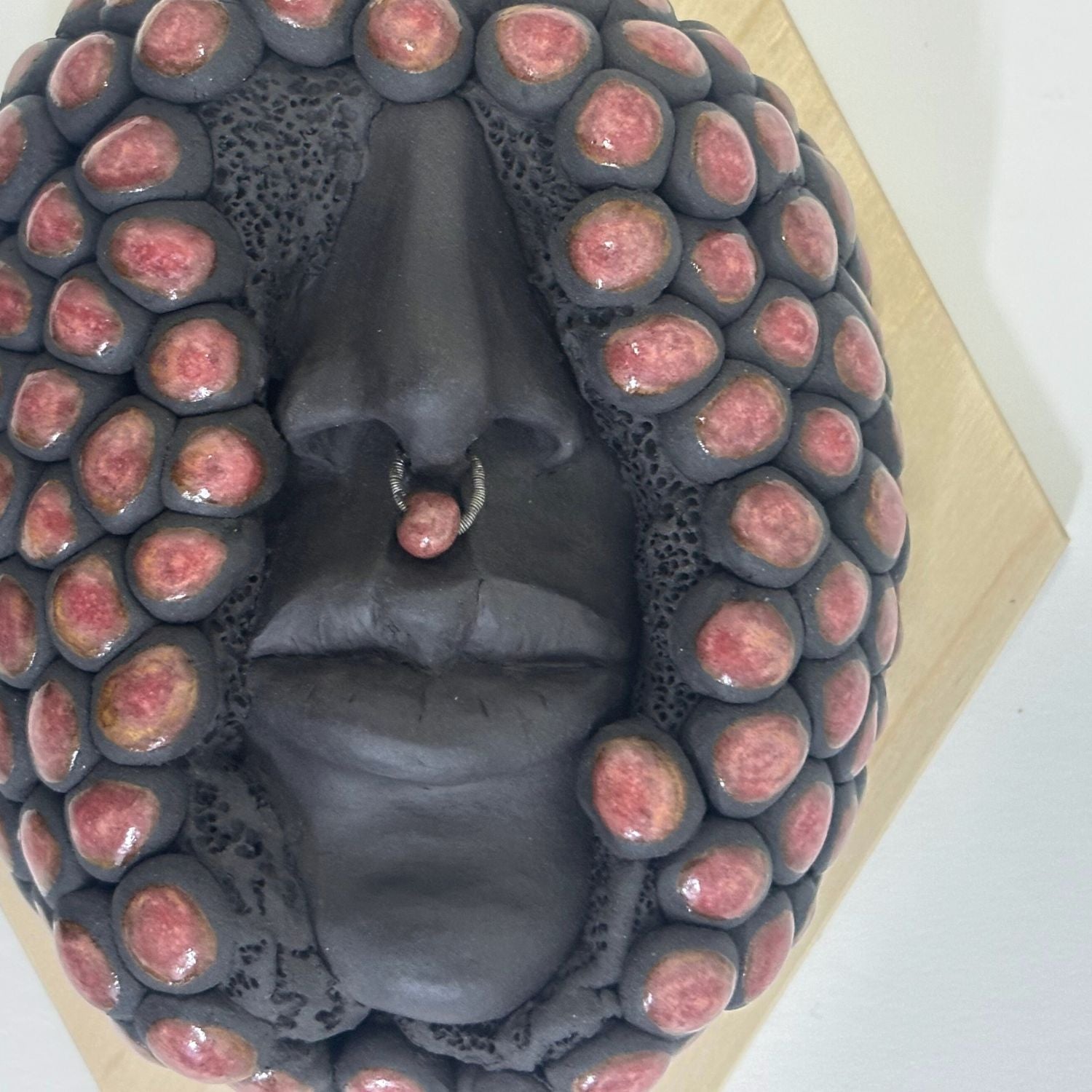 Surrealist black stoneware clay wall hanging combining facial features and berries