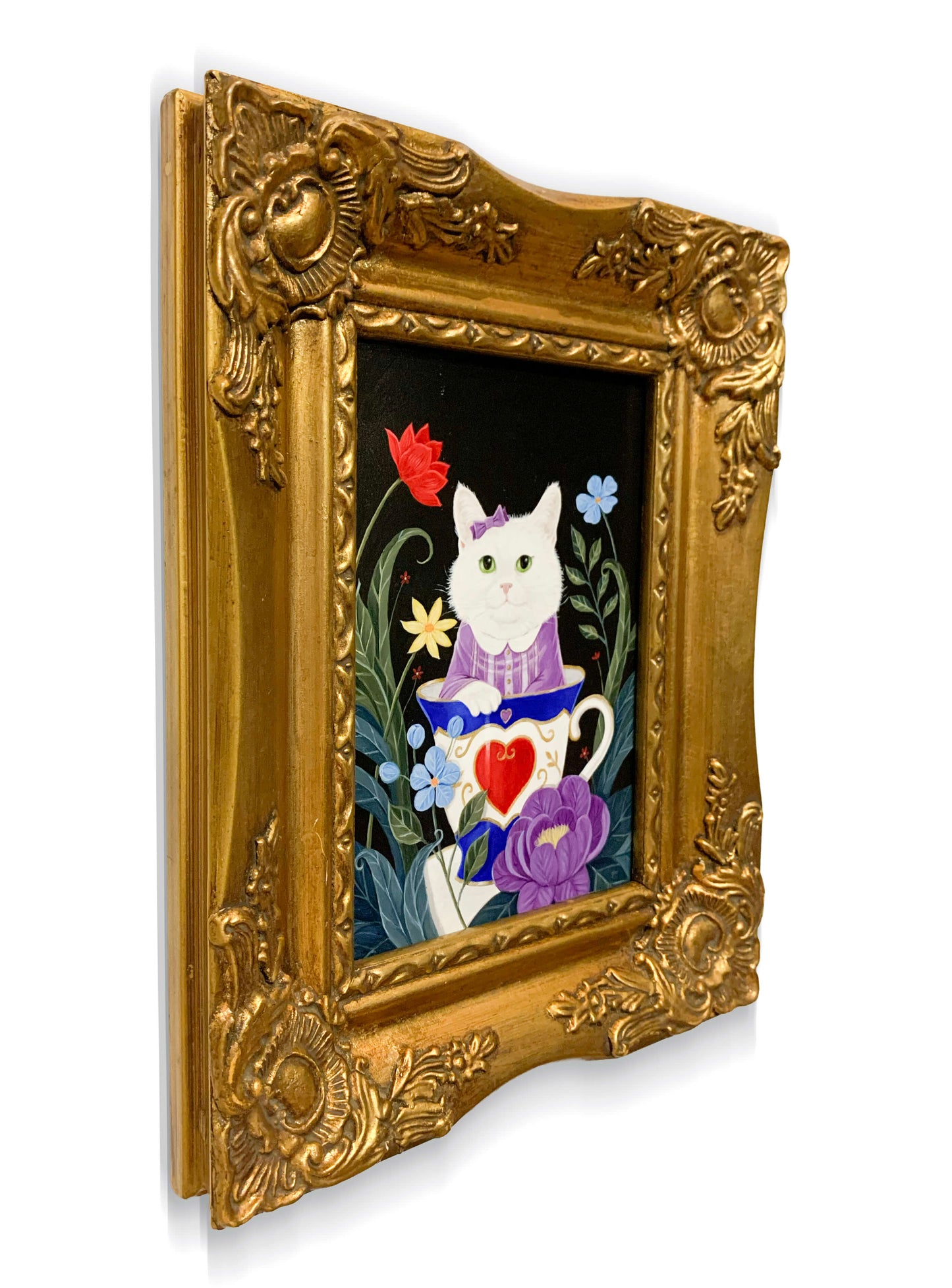 An ornate gold picture frame containing a colorful illustration of a white cat in a purple dress sitting in a teacup with flowers.