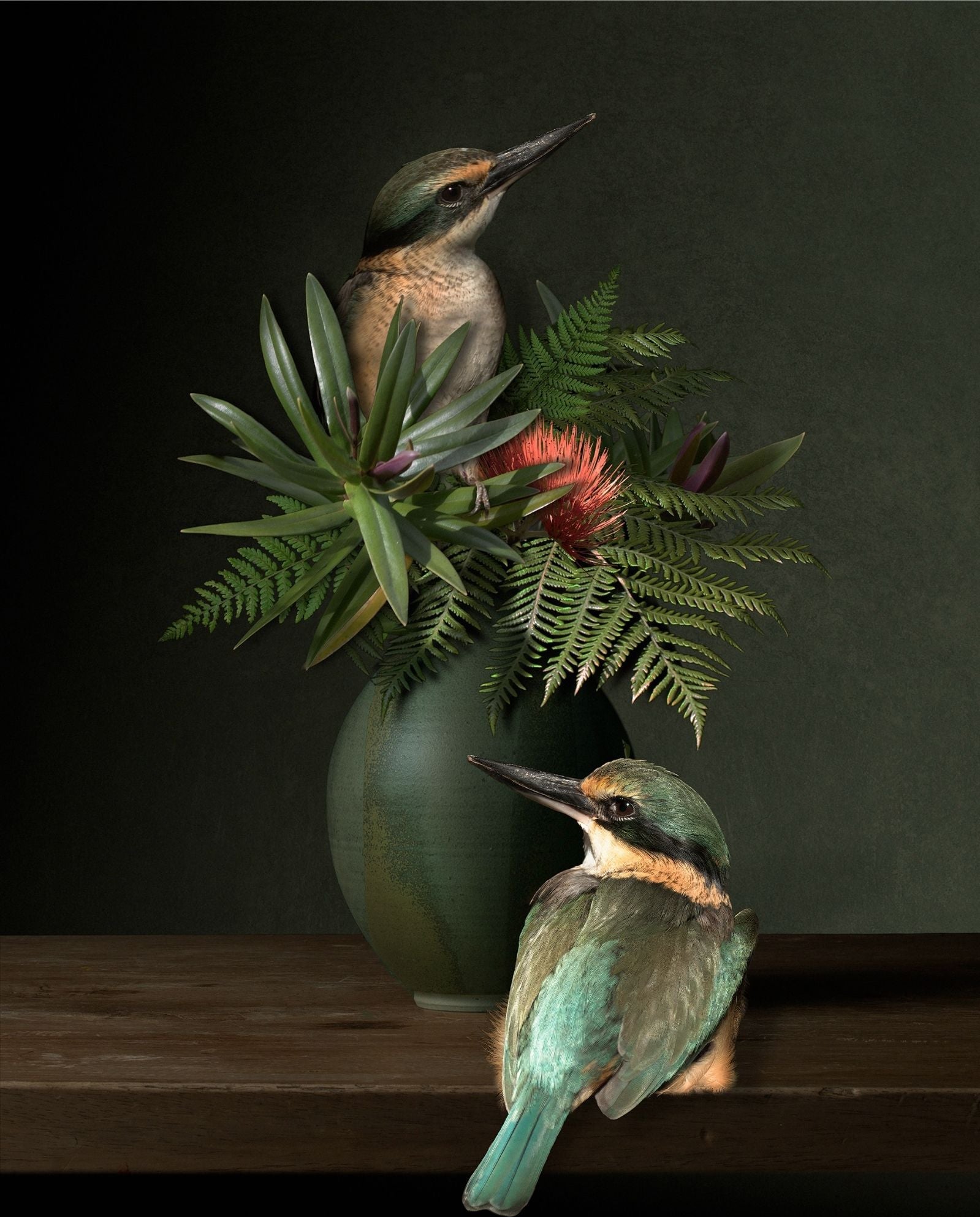 Two kingfishers perched on a wooden surface with a vase of flowers and leaves in the background.