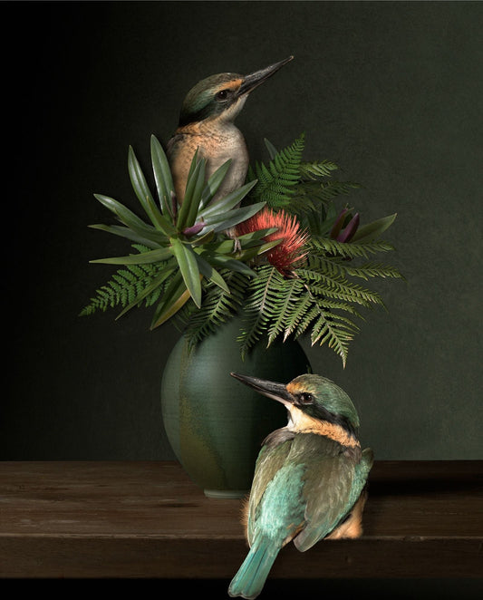 Two kingfishers perched on a wooden surface with a vase of flowers and leaves in the background.