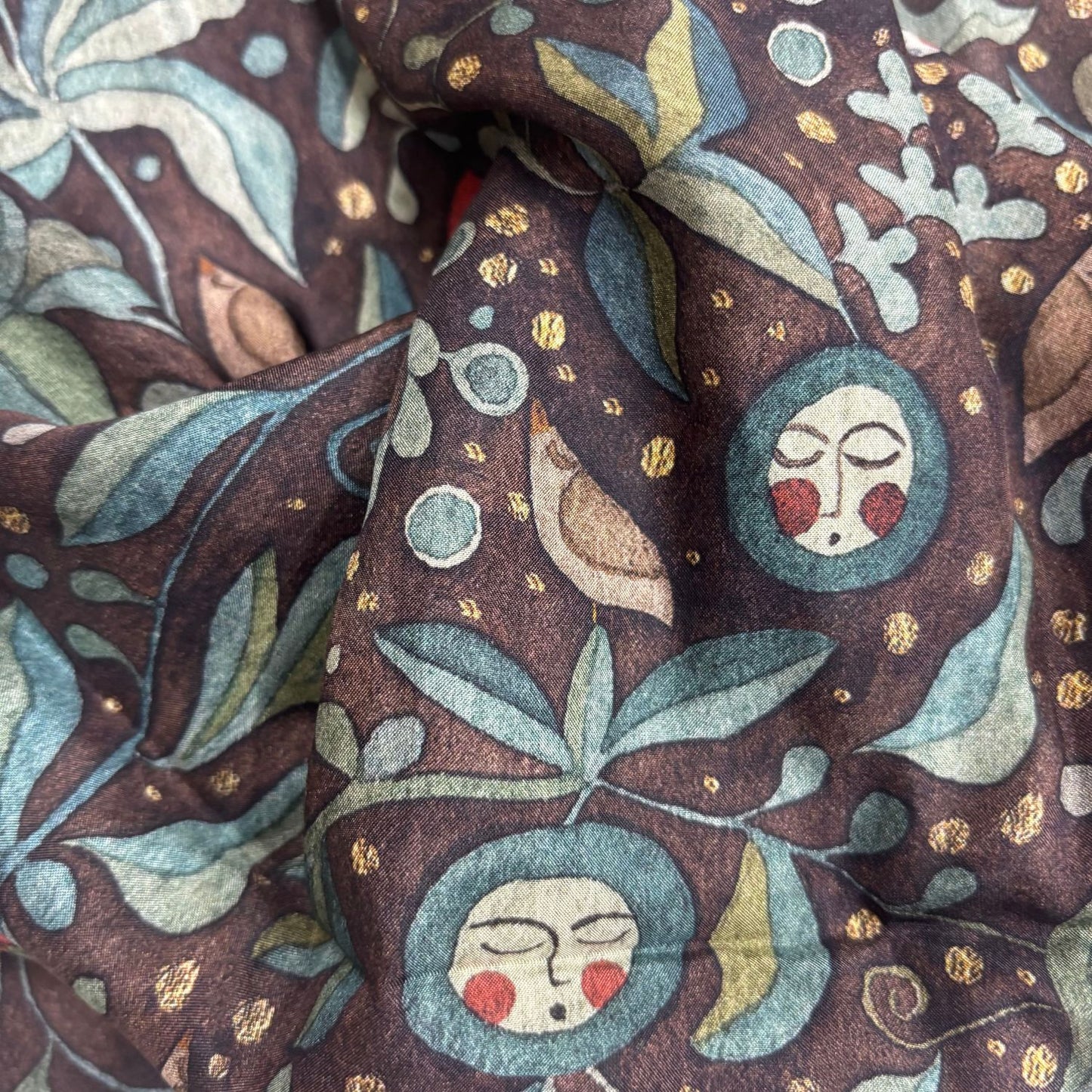 Close-up of fabric with decorative pattern featuring faces, leaves, and birds.