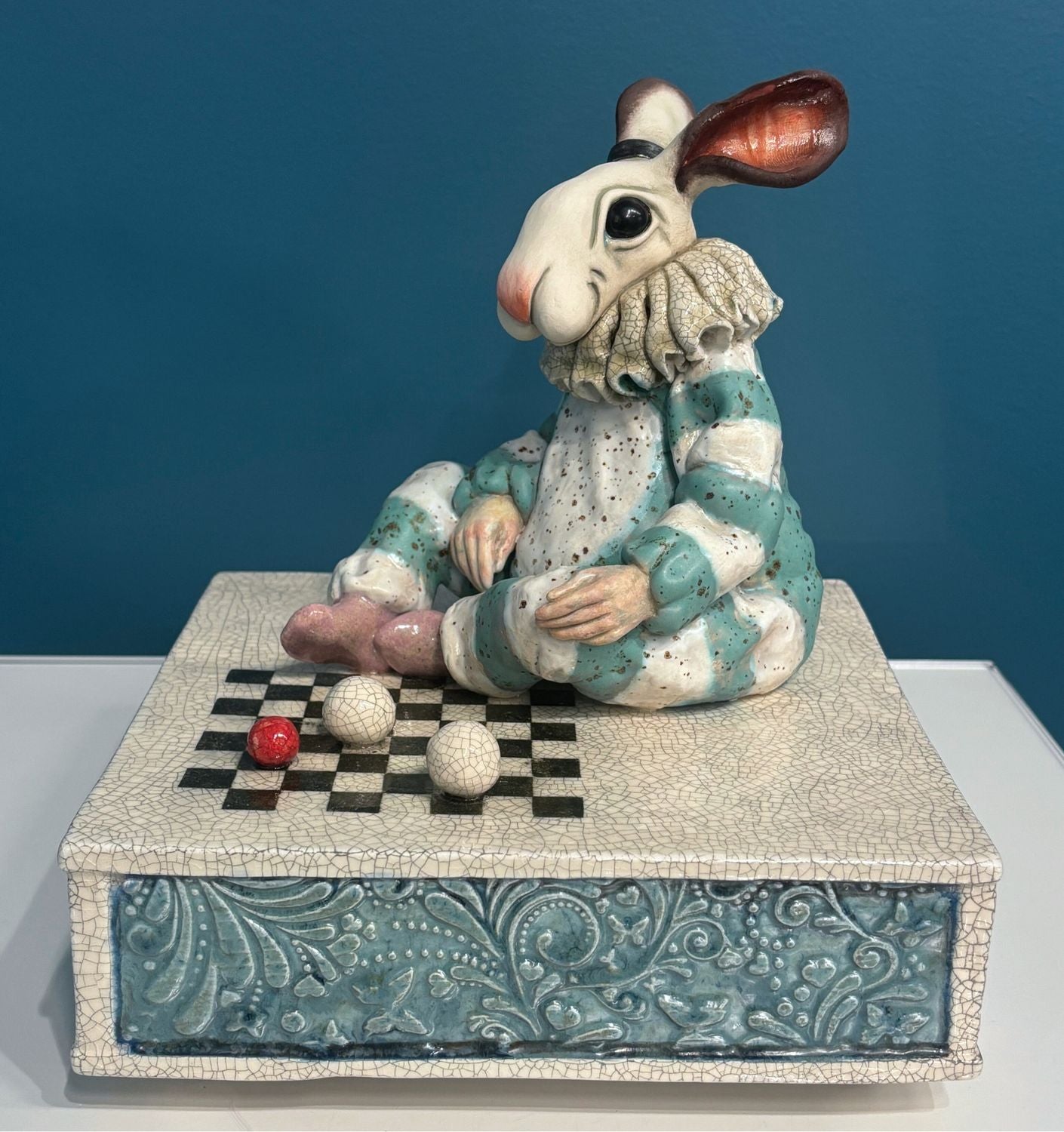 Ceramic rabbit figure playing checkers on a decorative box with a blue background