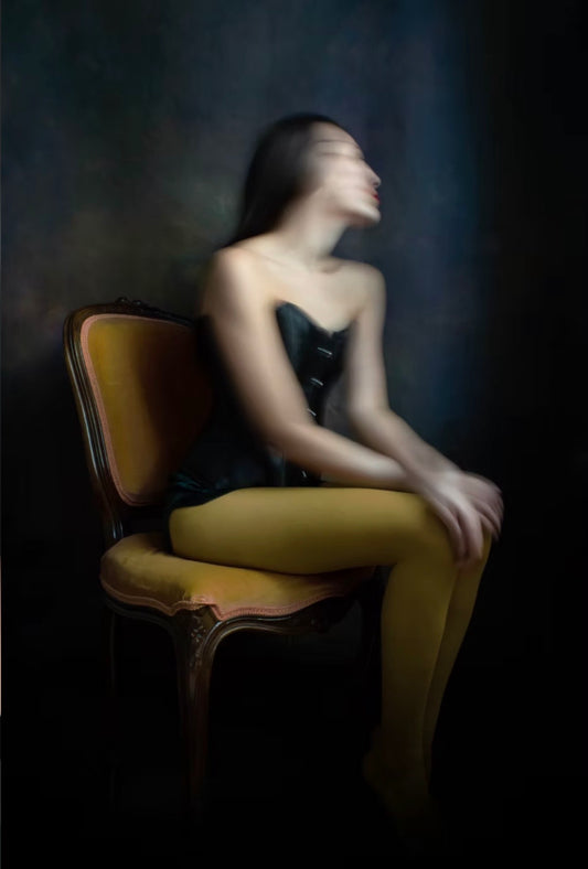 Woman sitting on a yellow chair with a blurred face against a dark background