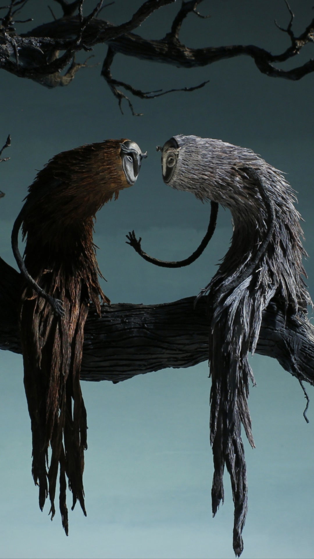 A surreal artwork showing two bird-like creatures perched on a tree branch, facing each other against a dark blue-gray background. One creature has brown feathers and a white beak, while the other has gray feathers and a curved black tail.