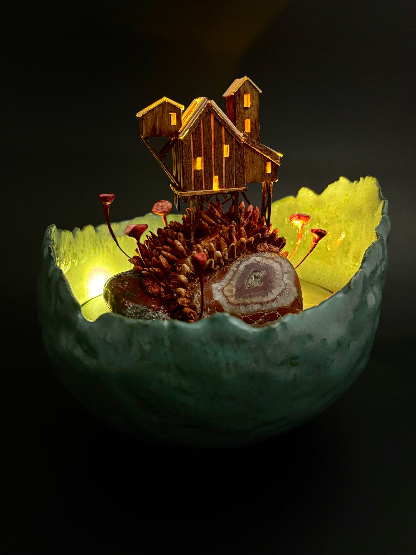 Small wooden cabin model inside a glowing green bowl on a dark background