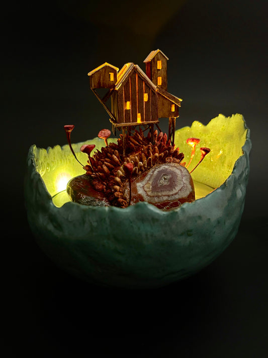 Small wooden cabin model inside a glowing green bowl on a dark background
