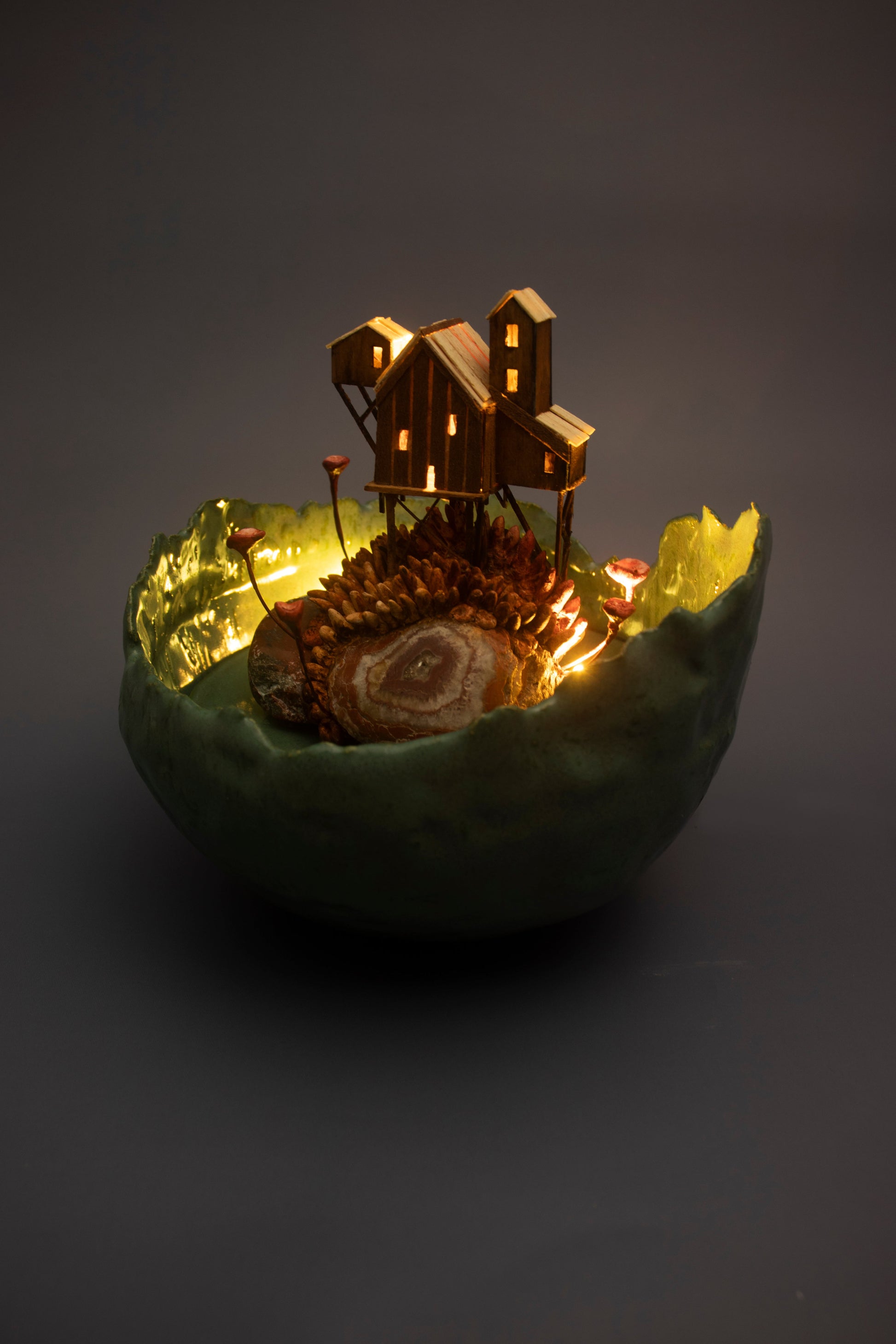 Decorative piece with a small house and lights inside a dark green shell on a gray background