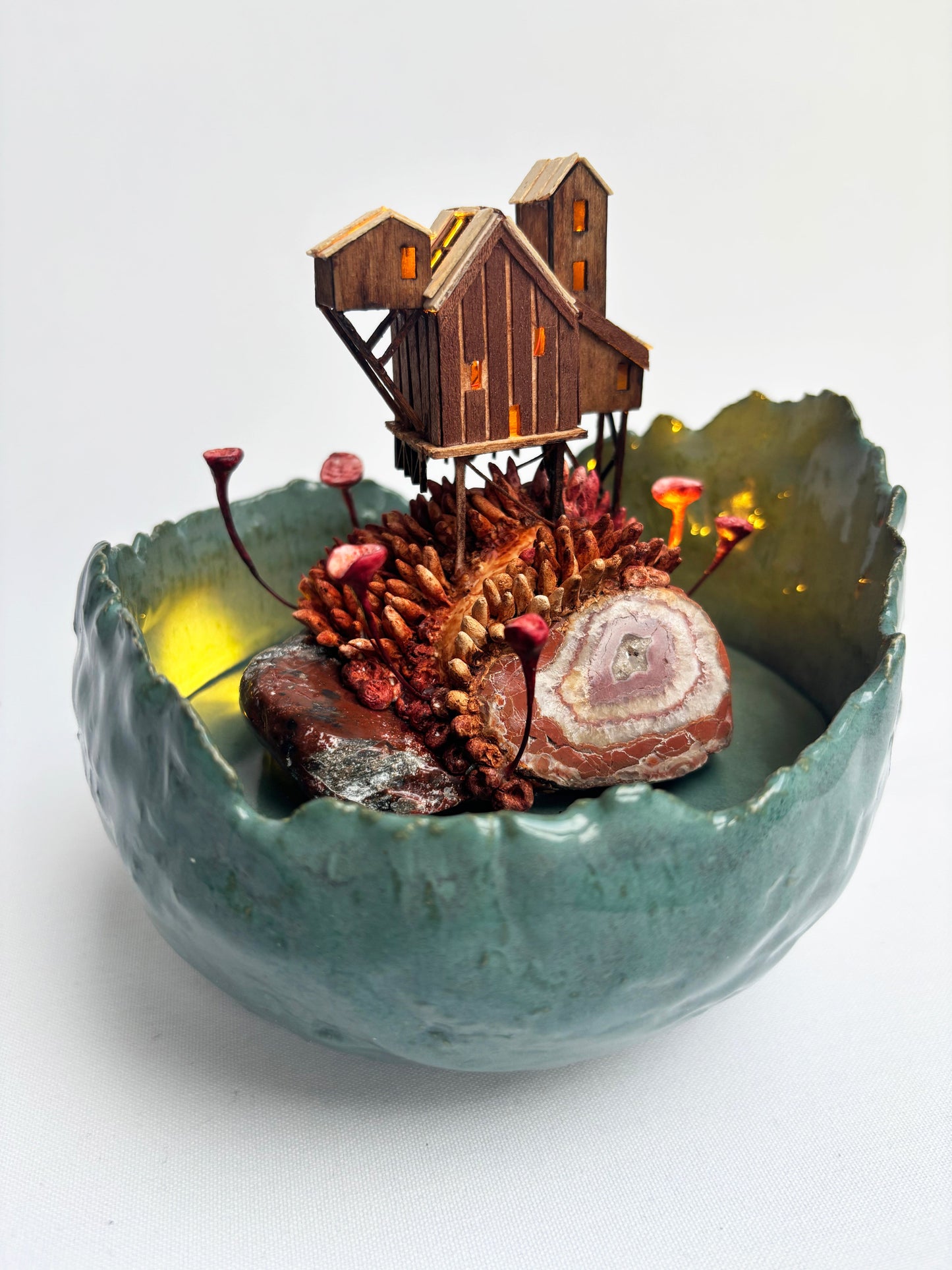 Decorative bowl with a miniature wooden cabin and natural elements on a white background